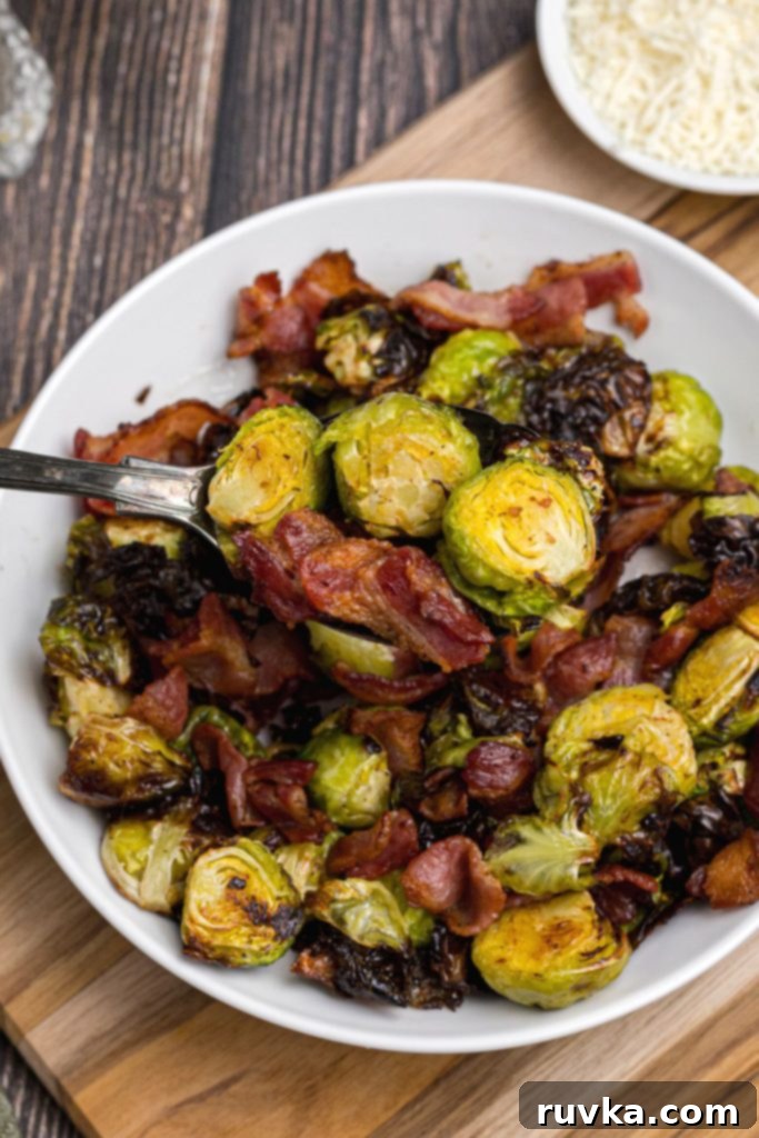 Crispy Air Fryer Brussels Sprouts and Bacon 10 Silver serving spoon filled with cooked crispy brussels sprouts and pieces of bacon.