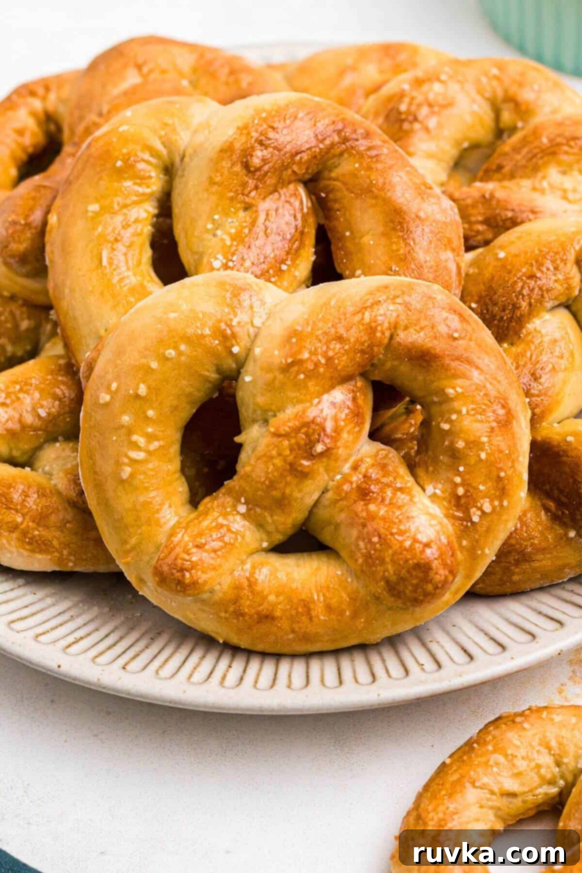 Perfectly Soft Air Fryer Pretzels 2 Golden brown soft pretzels on a round white plate with a bowl of melted cheese on a marble table.