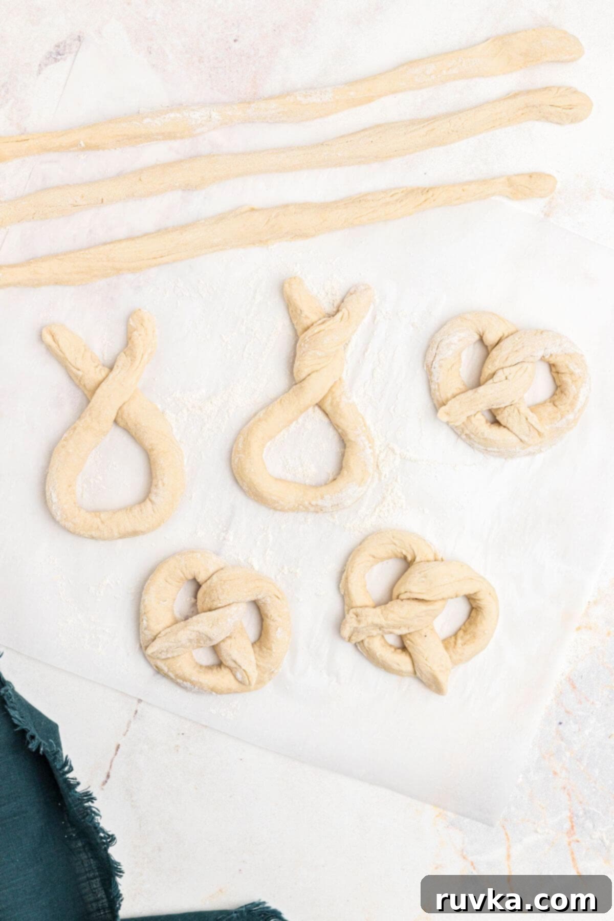Perfectly Soft Air Fryer Pretzels 7 Pretzel dough ropes being twisted into pretzel shapes on a marble surface.