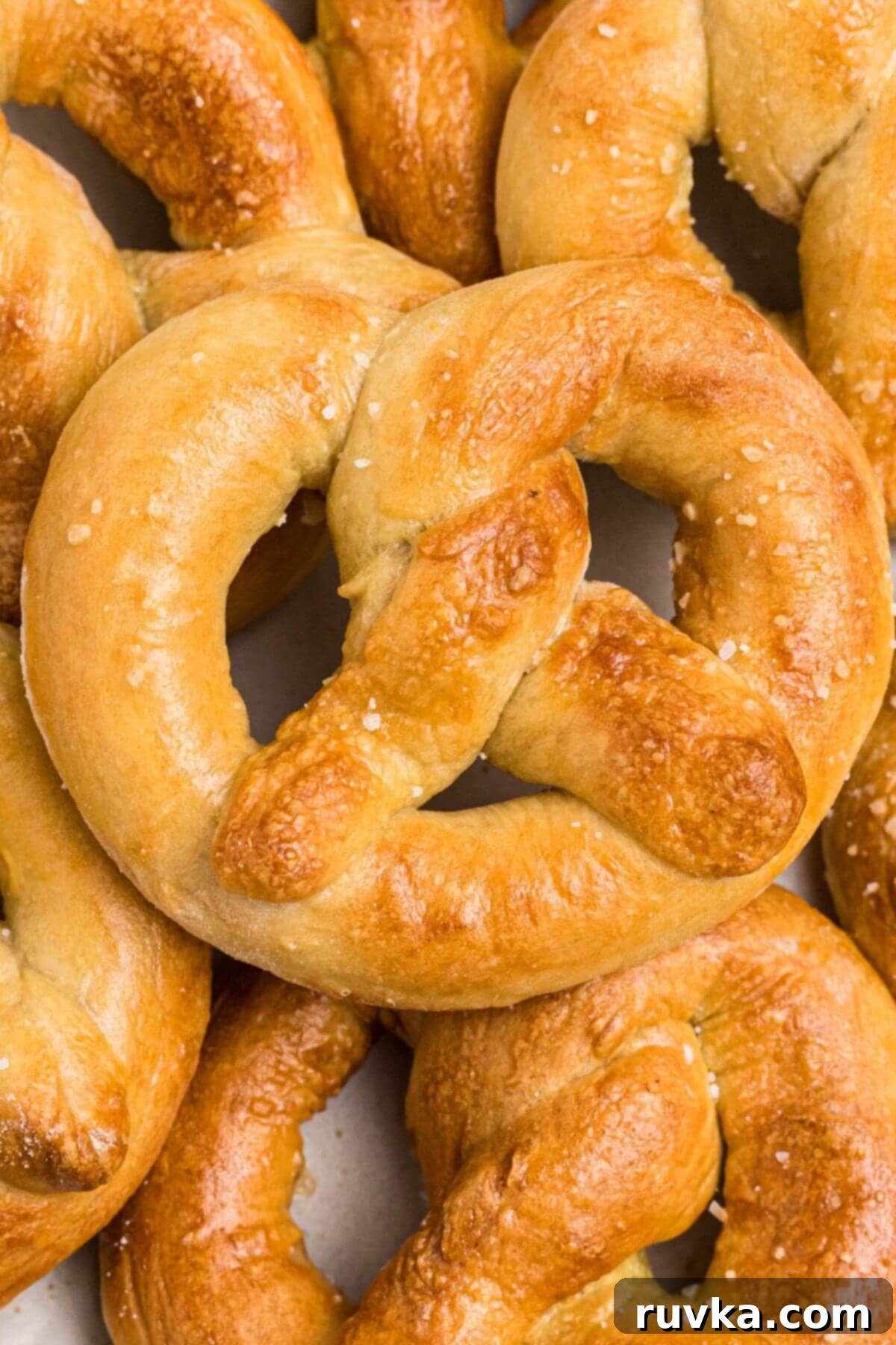 Perfectly Soft Air Fryer Pretzels 10 Golden soft pretzels stacked on a white plate and sprinkled with coarse salt.