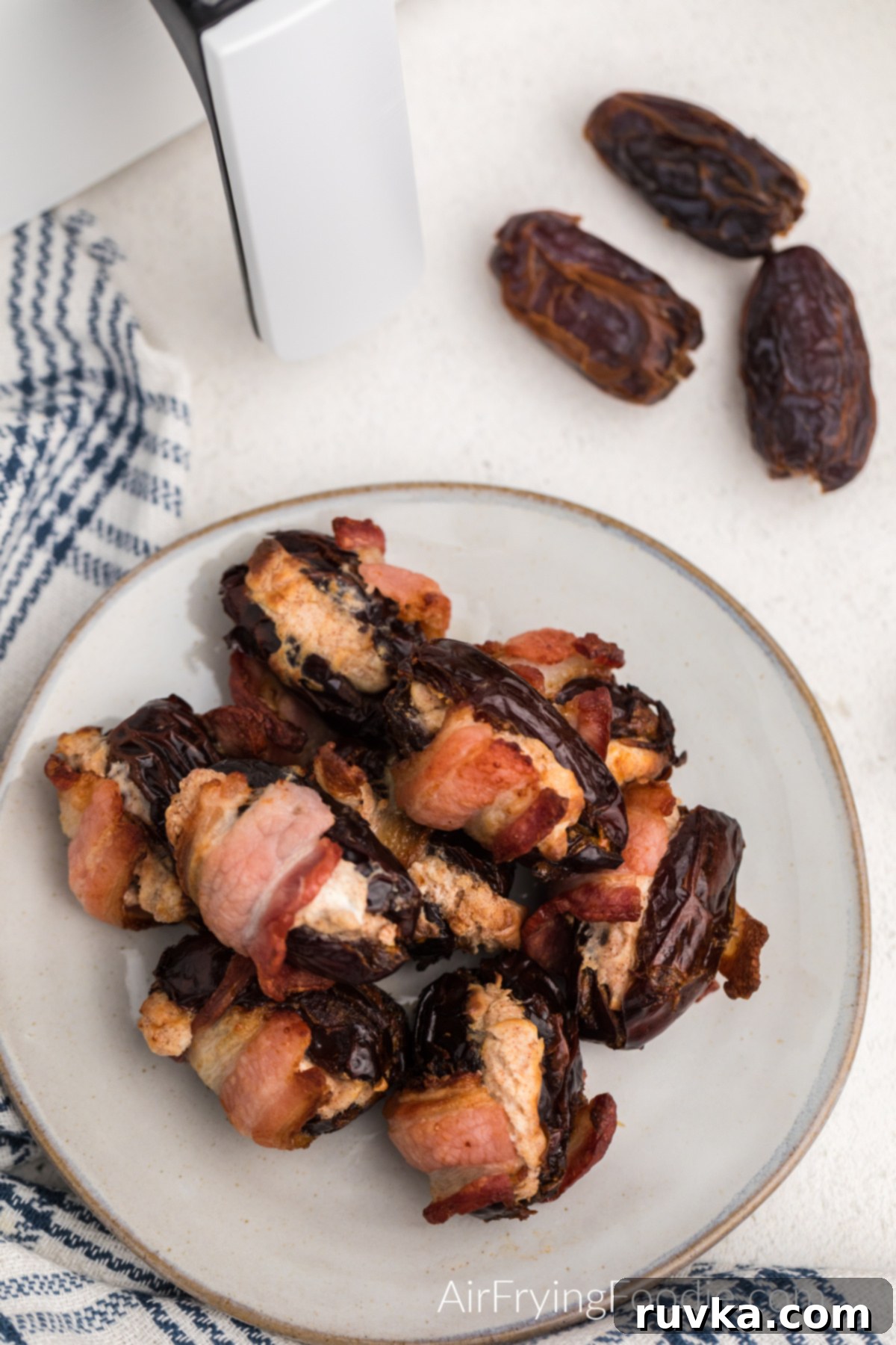 Crispy Air Fryer Bacon Wrapped Dates 2 Overhead photo of cream cheesed stuffed bacon wrapped dates on a plate.