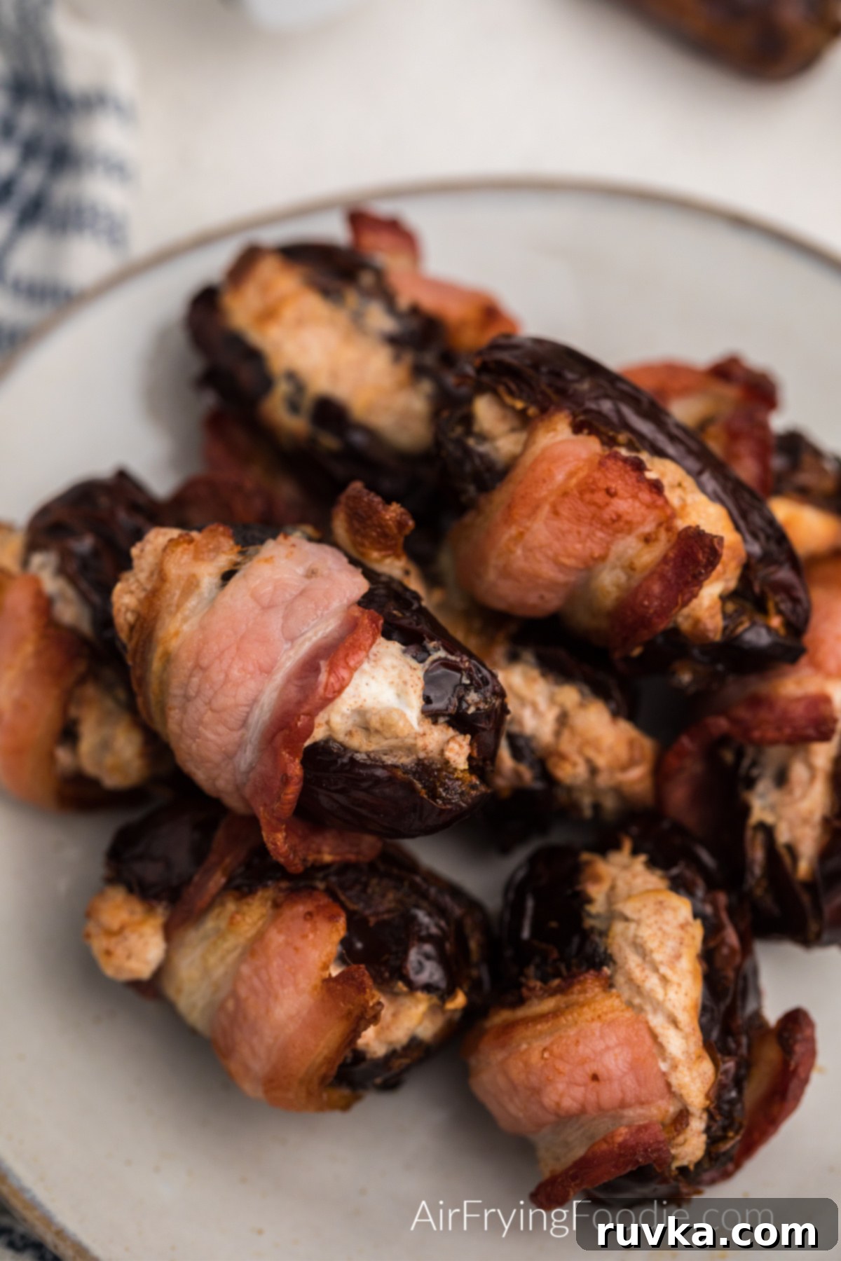 Crispy Air Fryer Bacon Wrapped Dates 10 Cream cheese stuffed air fryer bacon wrapped dates in a white plate, ready to serve.