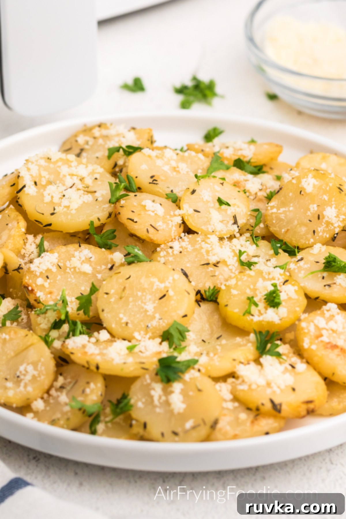 Golden Crispy Air Fryer Potatoes 2 Air fryer sliced potatoes served on a white plate topped with parmesan cheese and fresh chopped parsley. Golden brown and perfectly crispy.