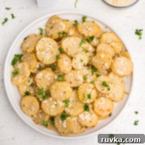 Golden Crispy Air Fryer Potatoes 11 Air fryer sliced potatoes on a white plate topped with parmesan and fresh chopped parsley, highlighting the golden crisp texture.