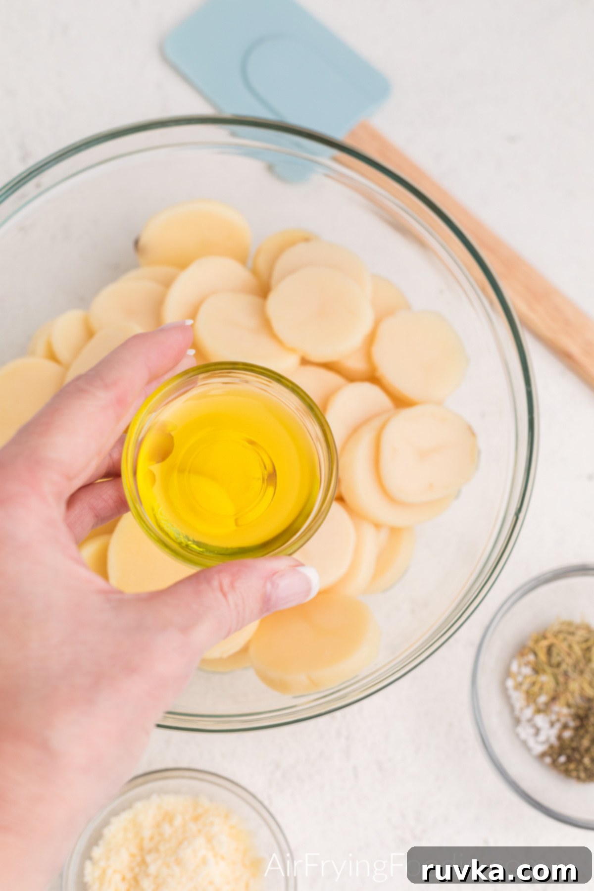 Olive oil being poured over a bowl of sliced potatoes, ensuring a thorough coating for even crisping.