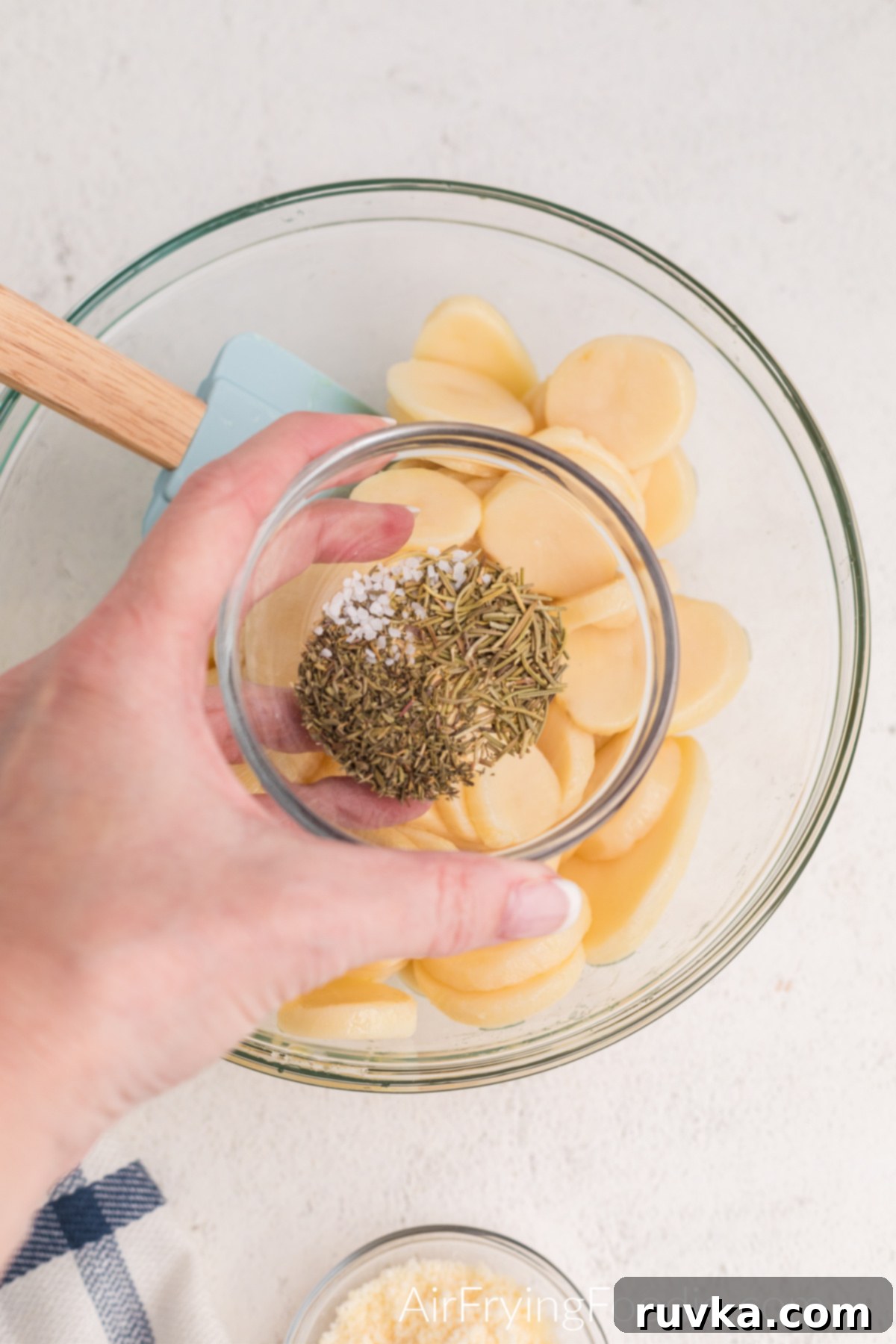 Seasonings in a small bowl being added to sliced potatoes, ready to be tossed for even distribution.
