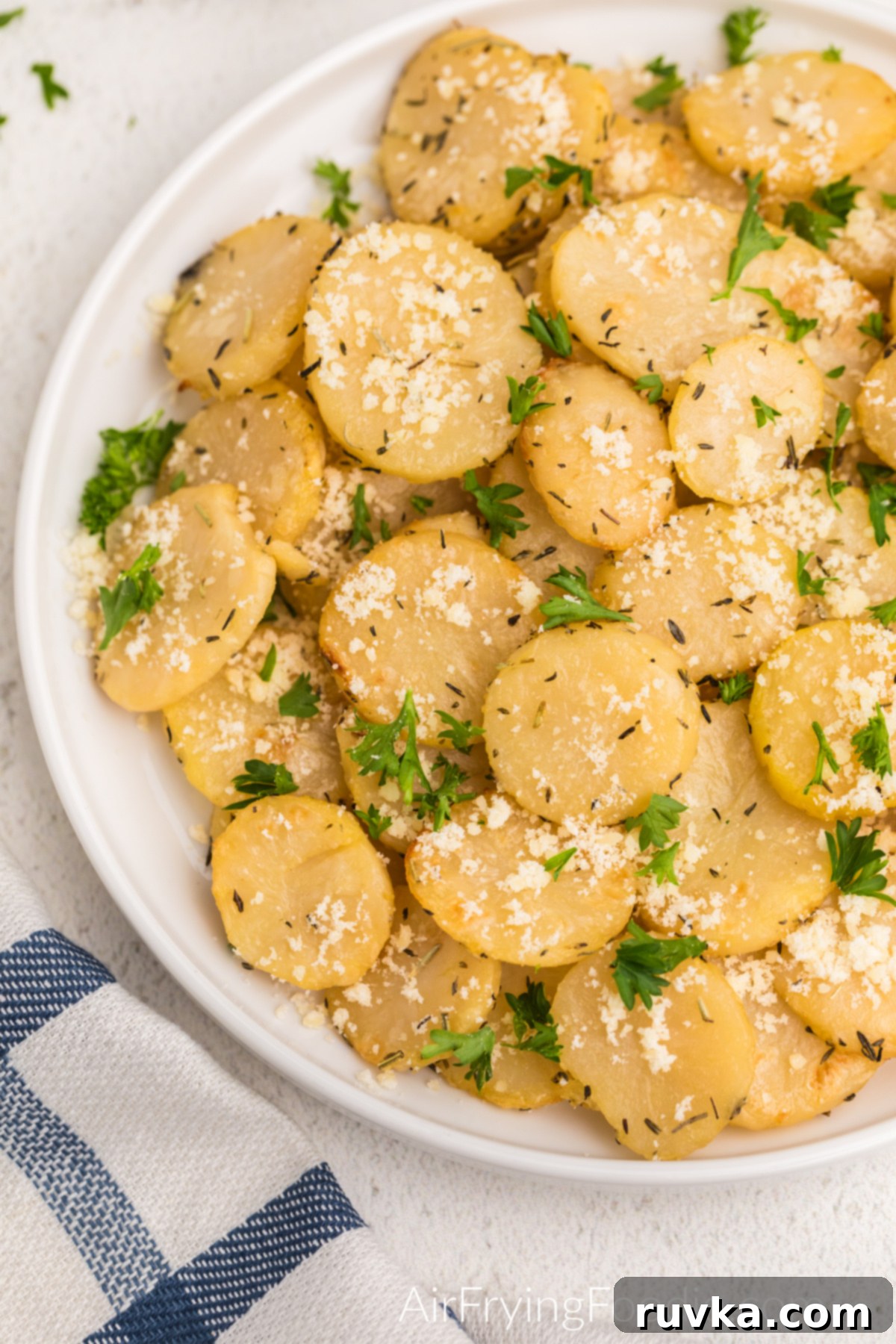 Air fried sliced potatoes covered with fresh parmesan cheese and fresh chopped parsley, ready to be enjoyed.
