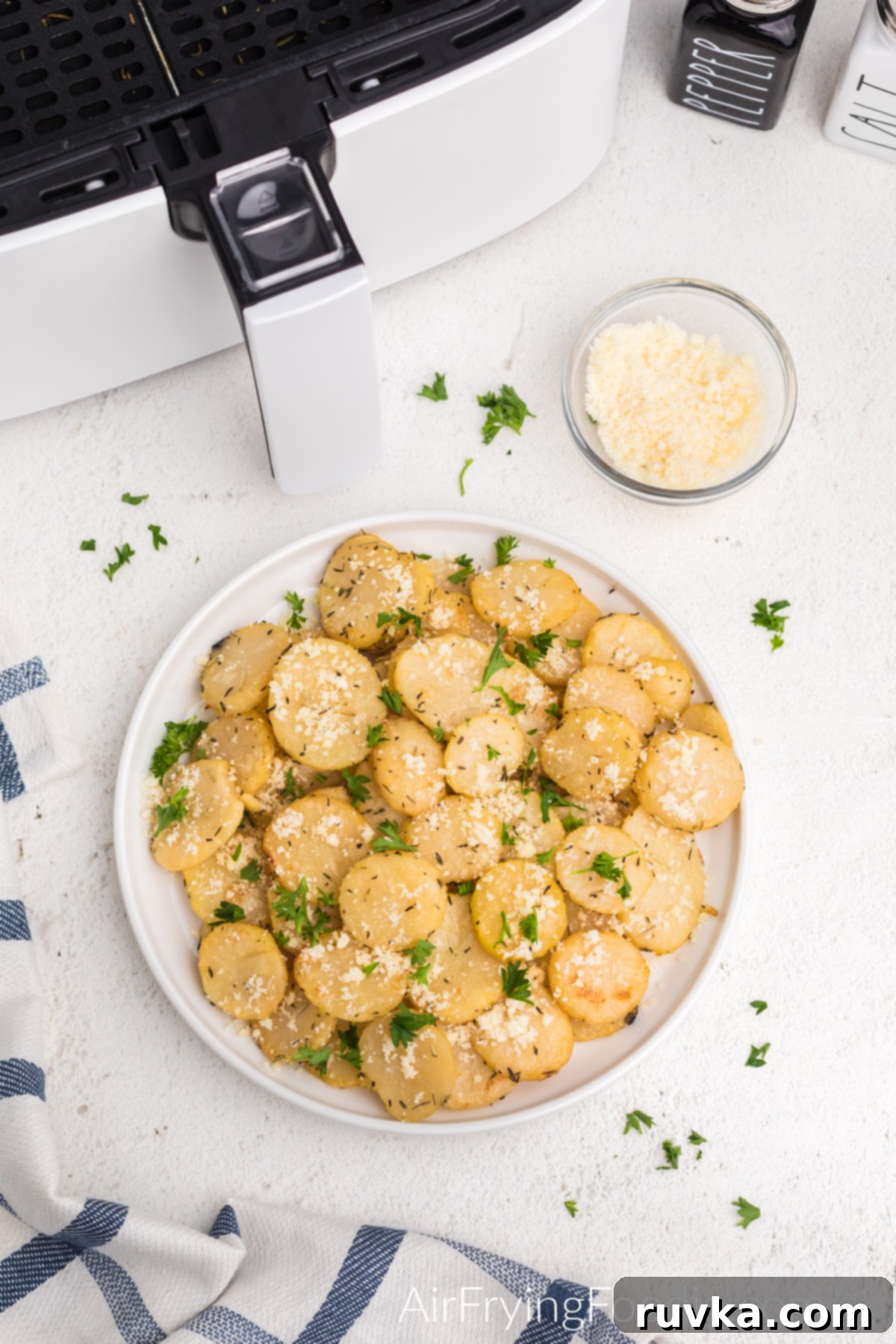 Golden Crispy Air Fryer Potatoes 10 Overhead photo of a white plate filled with crispy air fried sliced potatoes, garnished with fresh parmesan cheese and chopped parsley.
