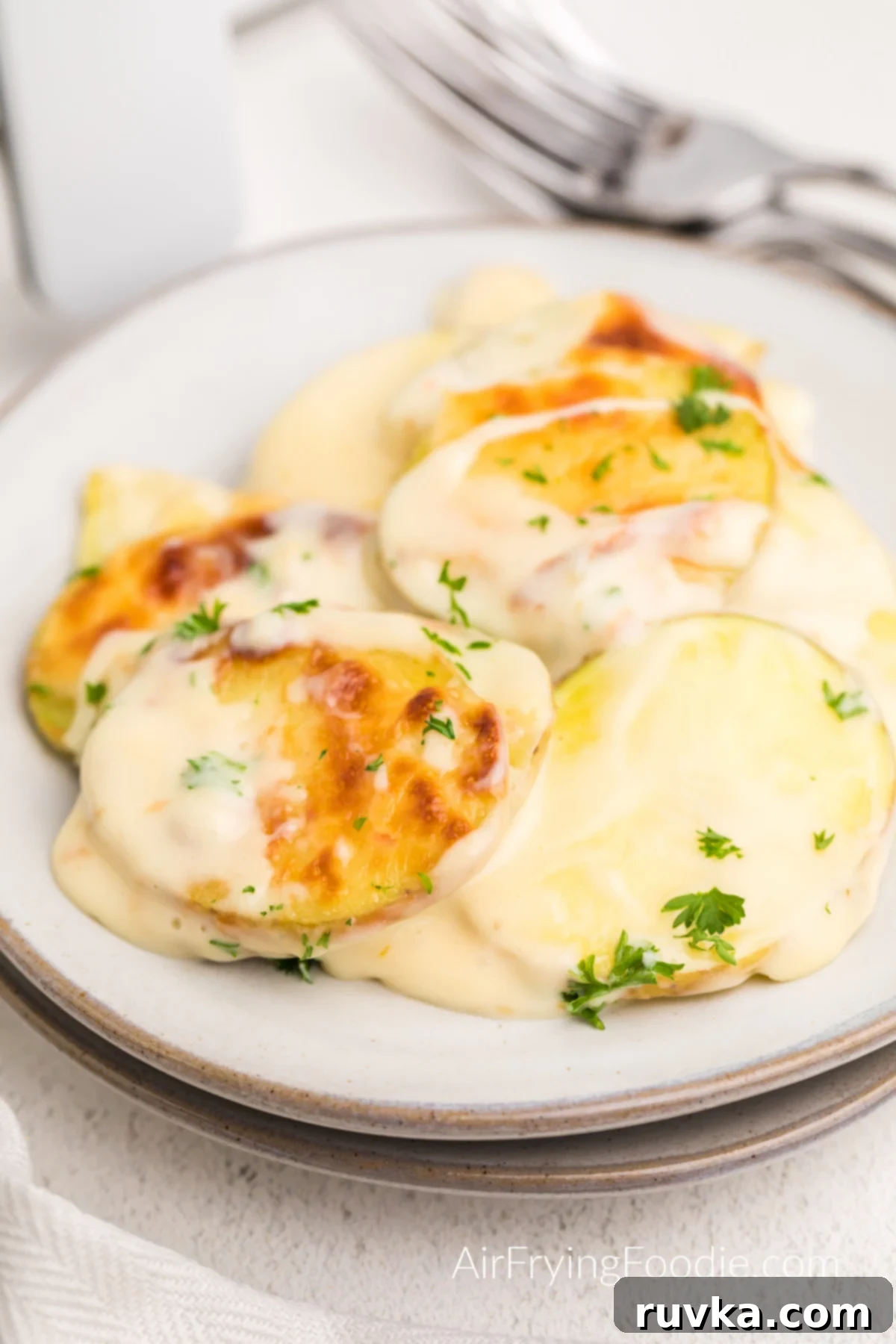 Easy Cheesy Air Fryer Scalloped Potatoes 2 Air fried scalloped potatoes served on a plate and topped with fresh parsley, highlighting the golden-brown cheese and tender potato layers.