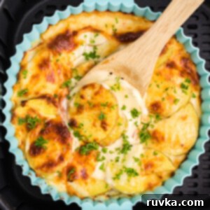 Easy Cheesy Air Fryer Scalloped Potatoes 14 Cheesy scalloped potatoes being scooped from the dish in the basket of the air fryer.