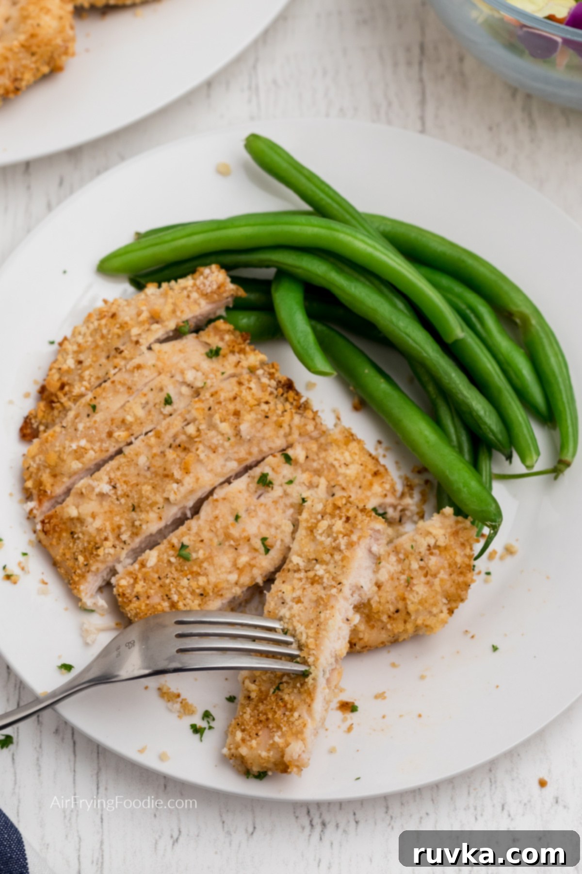 Crispy Air-Fried Chicken Breast 11 Sliced air fryer fried chicken with a fork taking a slice and a side of green beans on a white plate.