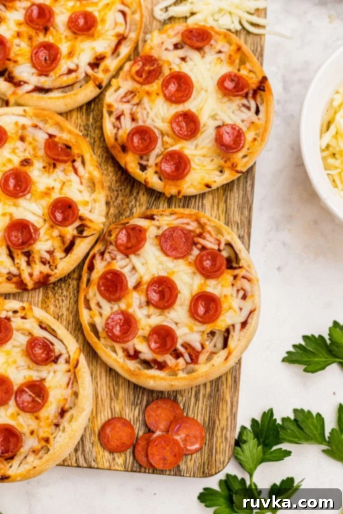Easy Air Fryer English Muffin Pizzas 2 Golden crispy English Muffin Pizzas on a rustic wooden cutting board, garnished with fresh basil.