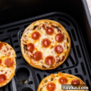 Easy Air Fryer English Muffin Pizzas 10 Golden crispy english muffin pizzas with melted cheese and cooked pepperonis in an air fryer basket.