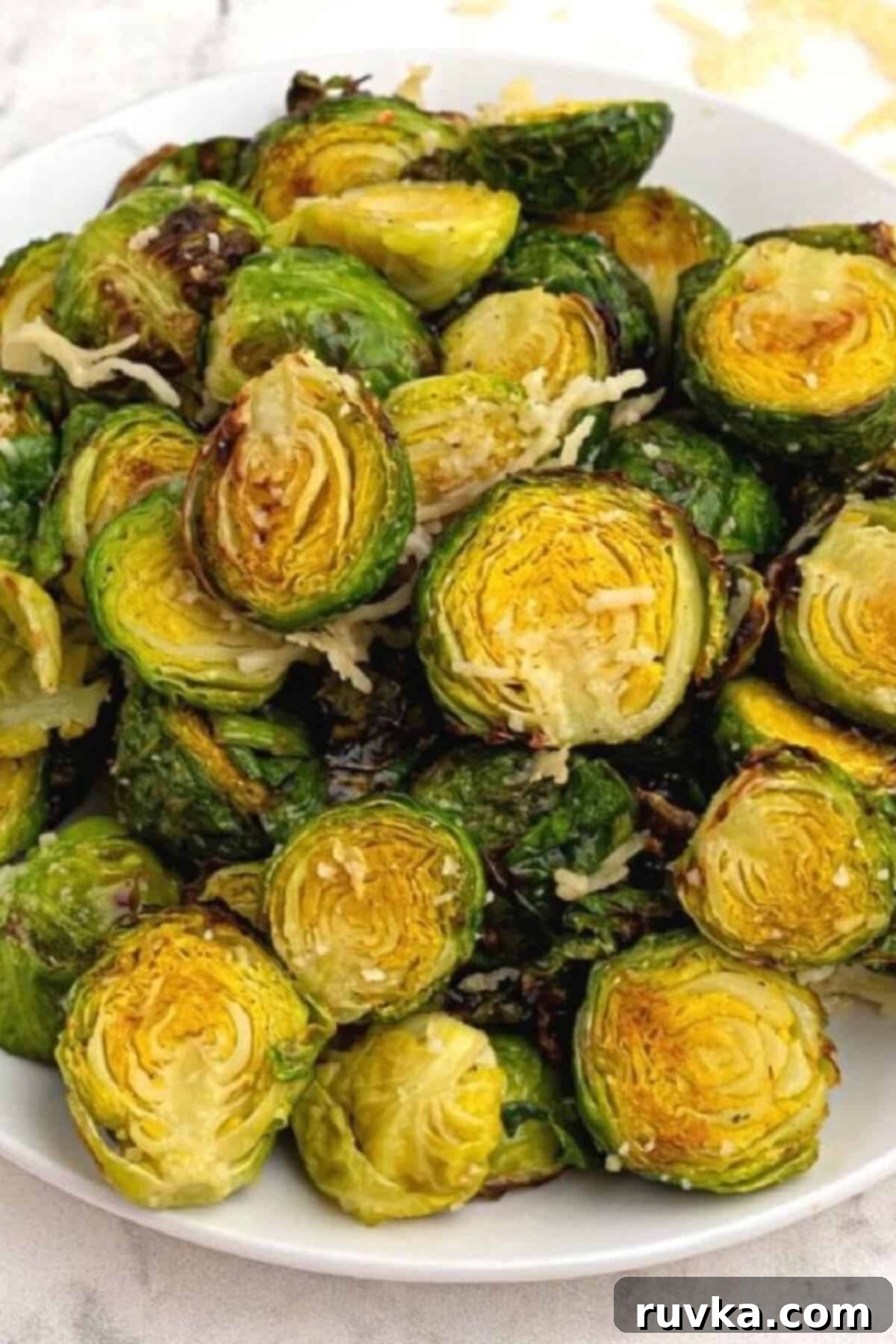 The Best Air Fryer Parmesan Brussels Sprouts 2 Close up of brussels sprouts on a white plate and topped with parmesan cheese.