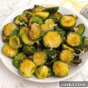The Best Air Fryer Parmesan Brussels Sprouts 8 Bright green and crispy brussel sprouts on a white plate sprinkled with parmesan cheese