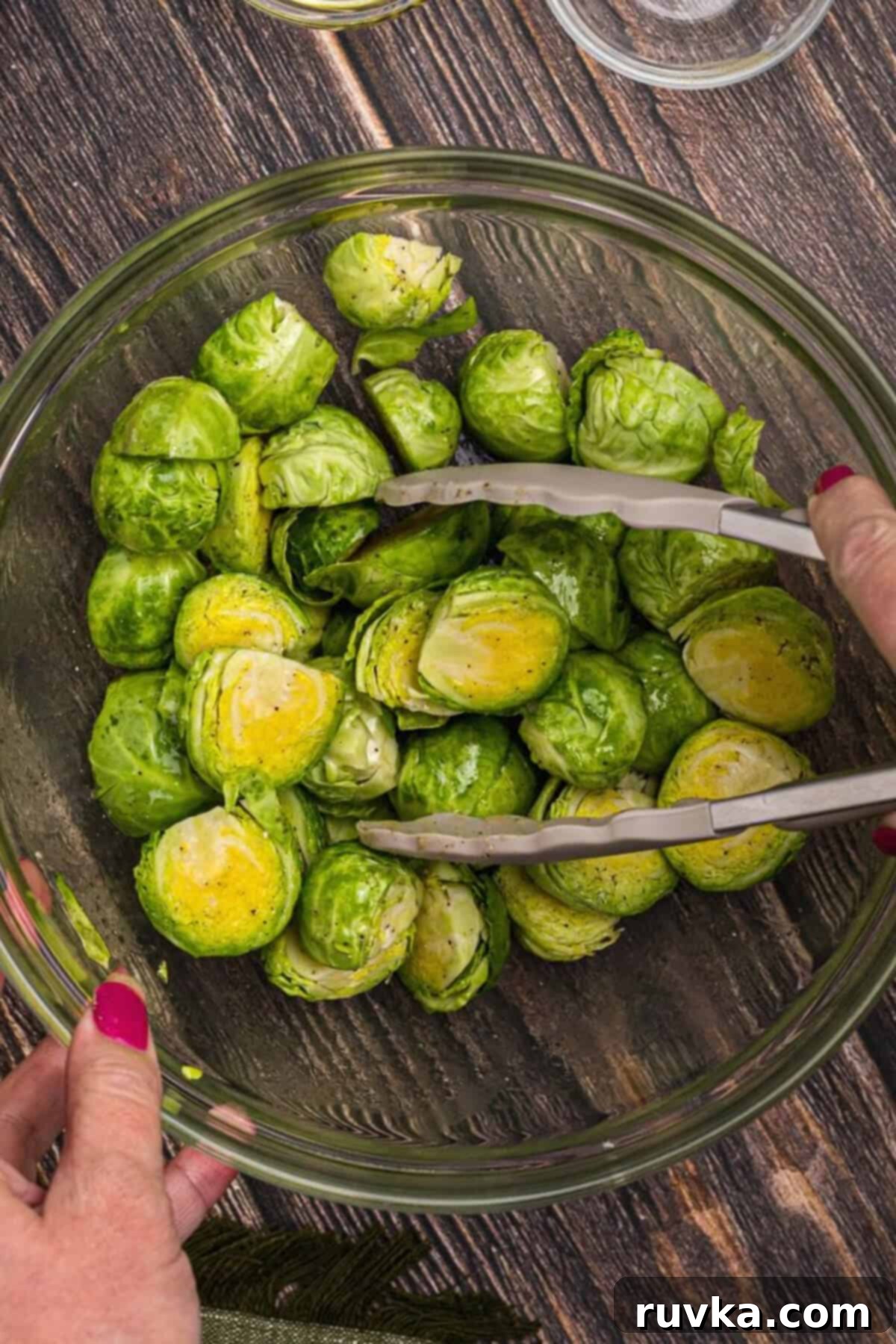 The Best Air Fryer Parmesan Brussels Sprouts 4 brussels sprouts in a bowl being tossed and coated with olive oil and seasonings.