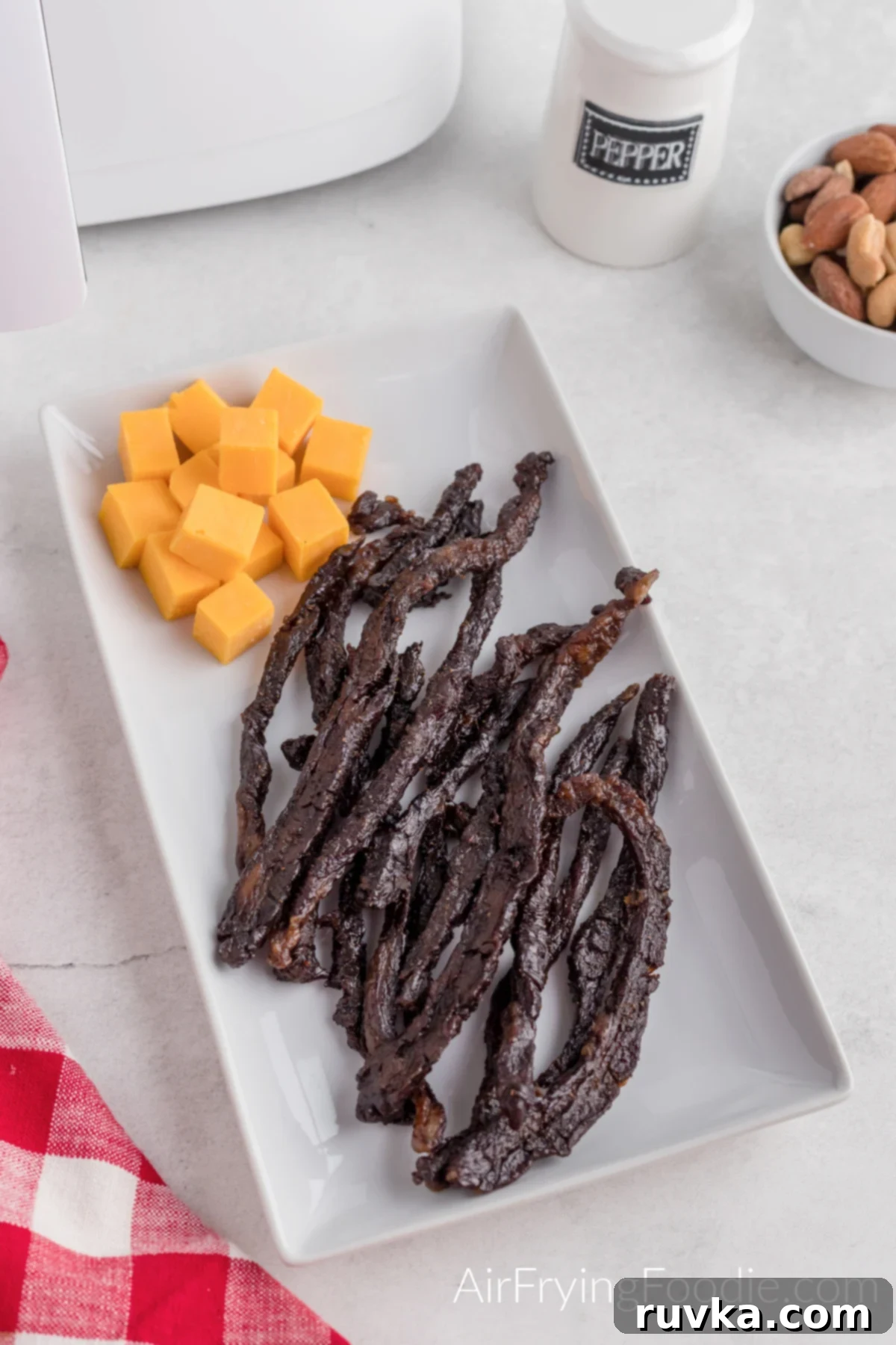 Homemade Air Fryer Jerky 2 Strips of air fryer beef jerky on a plate with cheese. Ready to eat.