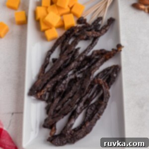 Homemade Air Fryer Jerky 11 Air fryer jerky on a white plate with blocks of cheese, ready to serve.