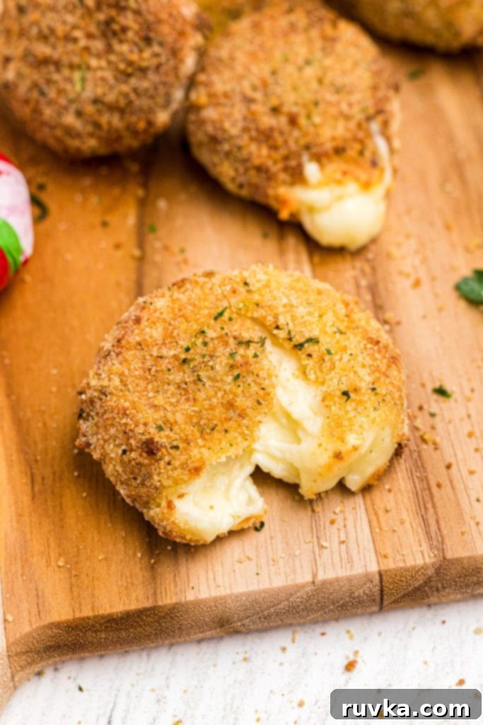Crispy Air Fried Babybel 2 Golden fried round piece of cheese, with breading on a wooden cutting board.