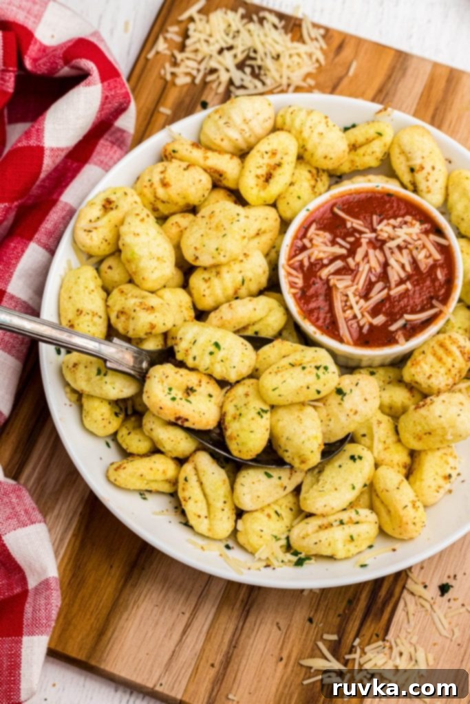 Crispy Air-Fried Gnocchi 2 Crispy air fried golden gnocchi on a white plate with mozzarella sauce, garnished with herbs.