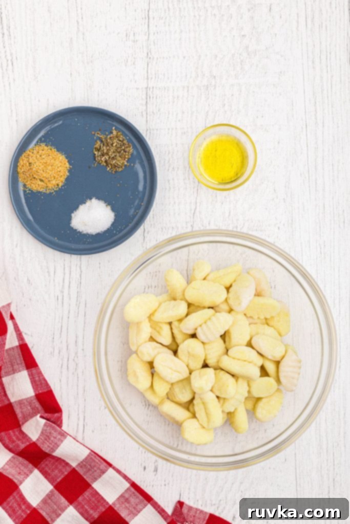Crispy Air-Fried Gnocchi 3 Uncooked gnocchi in a clear glass bowl, with olive oil and a small bowl of seasonings nearby, ready for preparation.