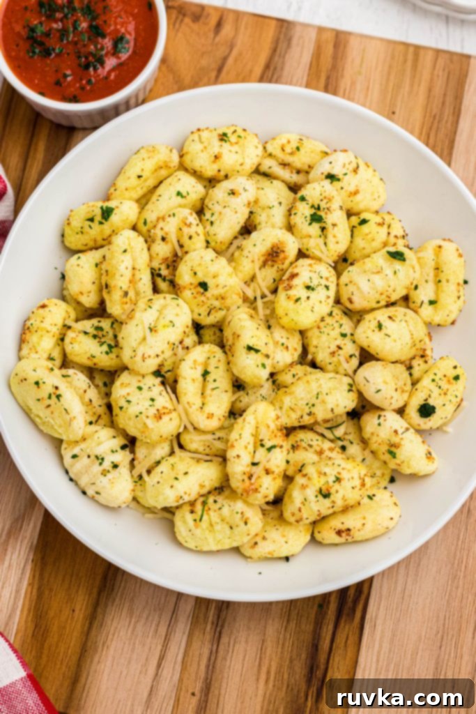 Crispy Air-Fried Gnocchi 7 Golden crispy seasoned gnocchi in a white bowl with marinara sauce on a rustic wooden cutting board, garnished with fresh herbs.