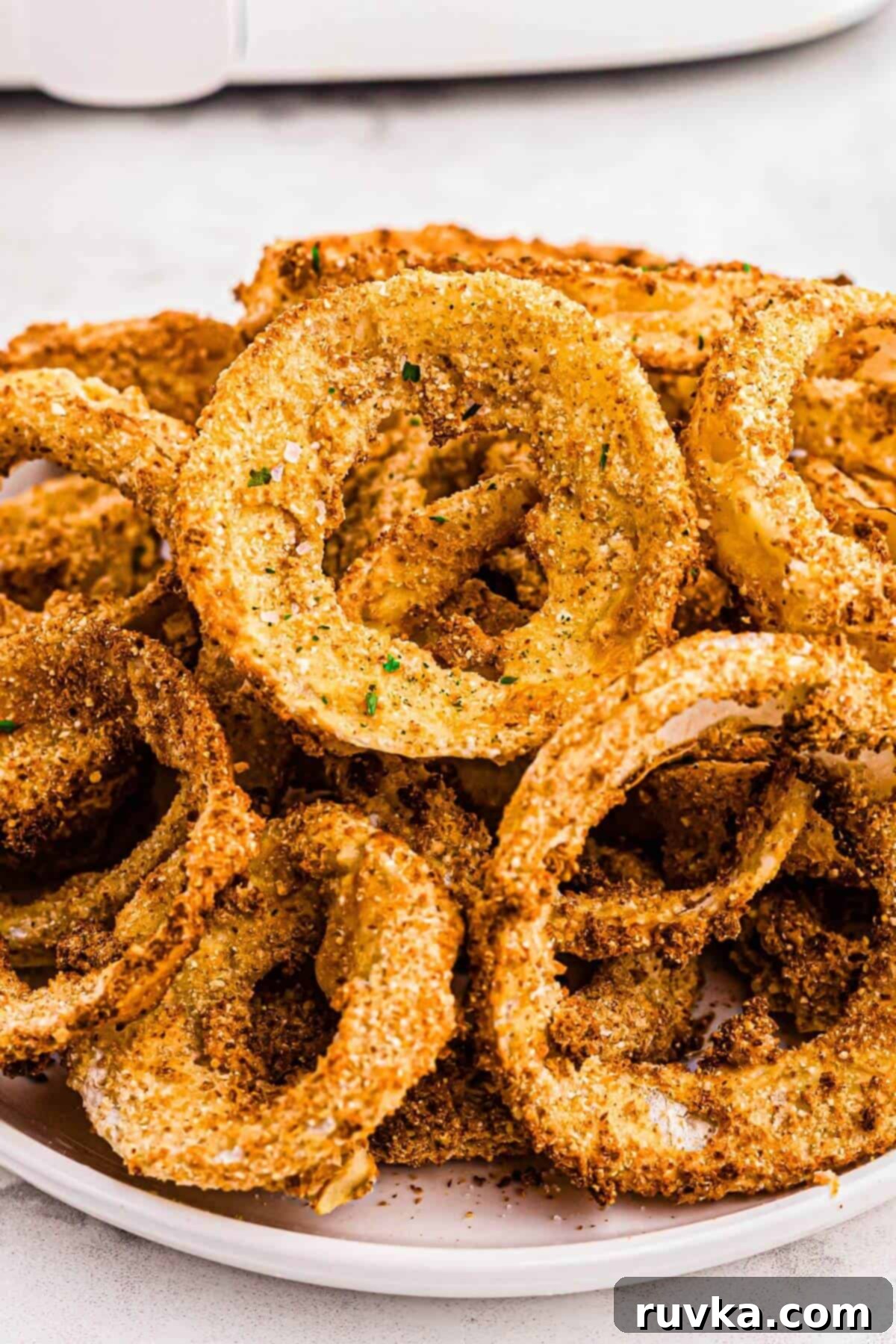 Guilt-Free Air-Fried Onion Rings 2 Golden crispy battered onion rings stacked on a white plate.