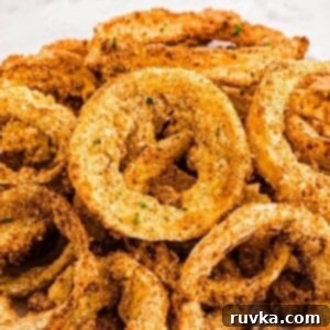 Guilt-Free Air-Fried Onion Rings 10 Golden crispy battered onion rings stacked on a white plate.