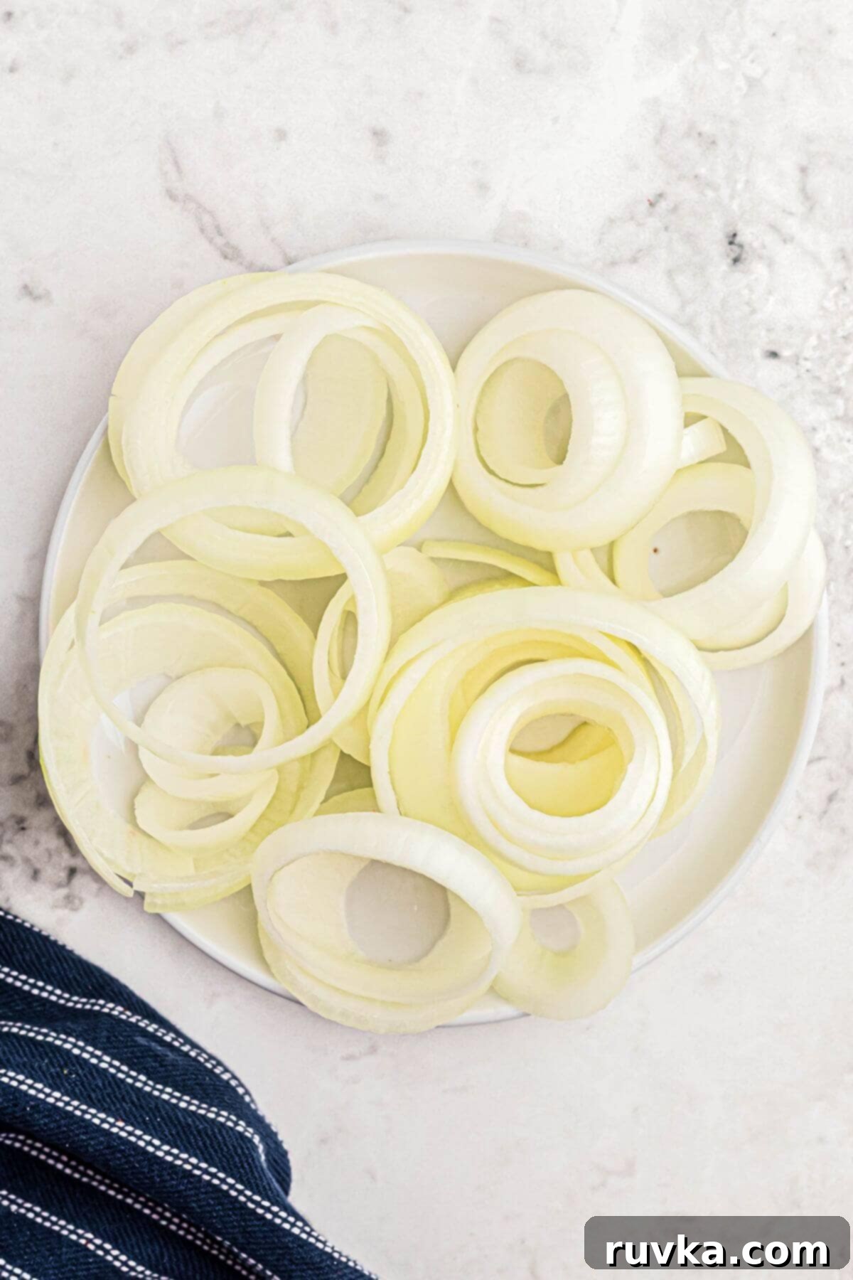 Guilt-Free Air-Fried Onion Rings 4 An onion sliced into rings, stacked on a white plate.