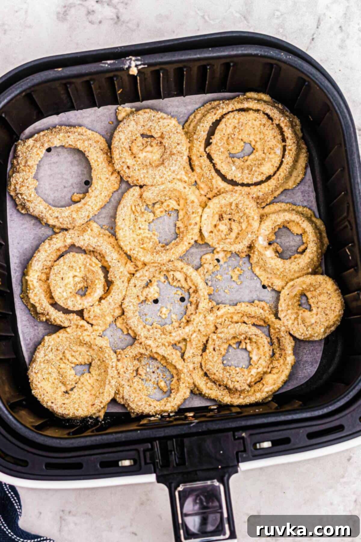 Guilt-Free Air-Fried Onion Rings 7 Uncooked battered onion rings in the air fryer basket, lined with parchment paper.