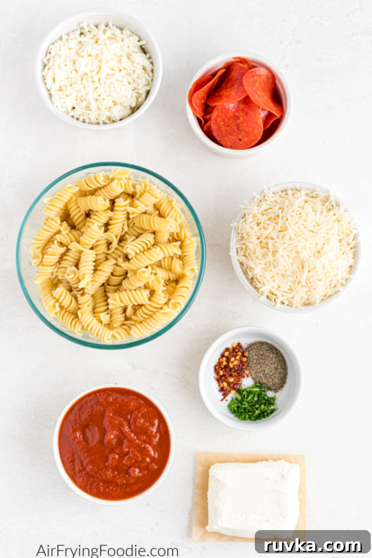 Air Fryer Pizza Pasta Bake 3 Ingredients needed to make pizza pasta casserole in the air fryer. Pasta noodles in a bowl, shredded cheese in a bowl, pizza sauce, cream cheese, and seasonings in a bowl.