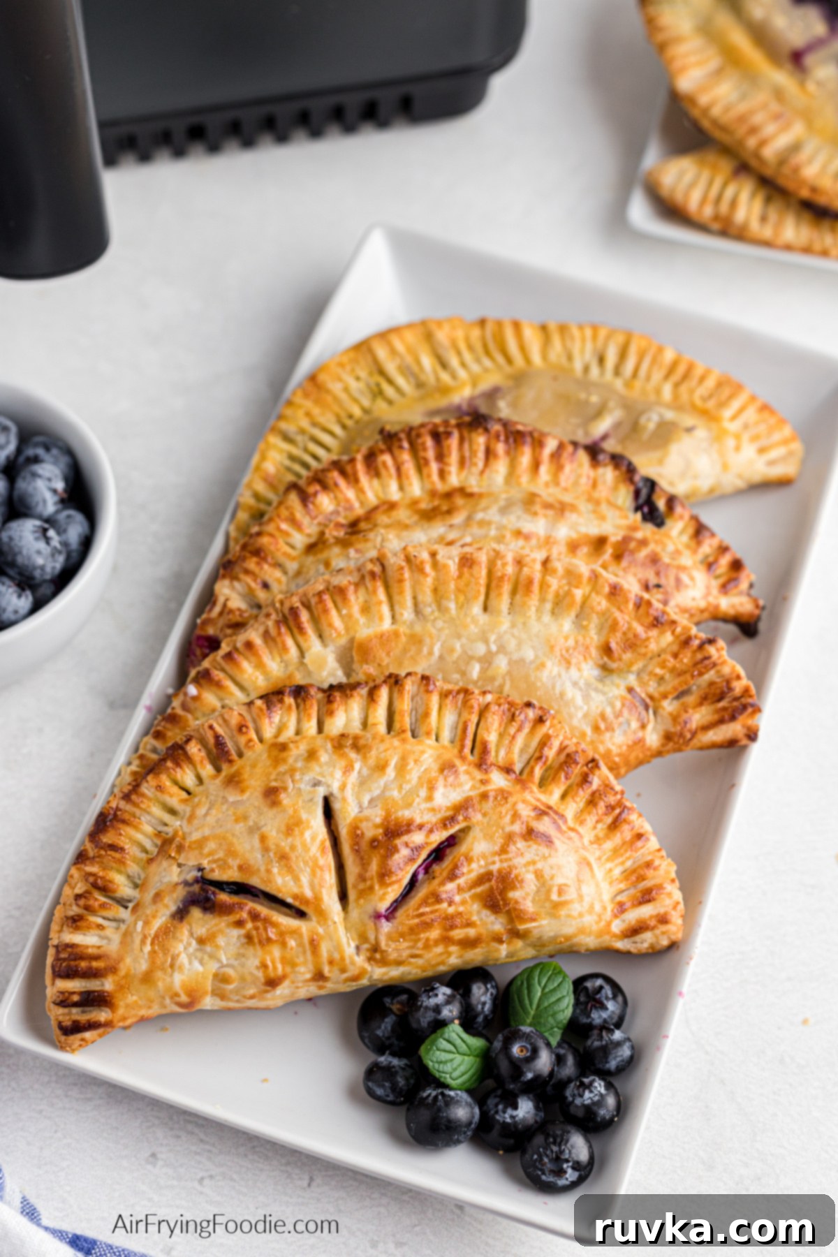 Crispy Air Fried Blueberry Pockets 13 Air fryer blueberry hand pies on a plate with a side of blueberries, ready to eat.
