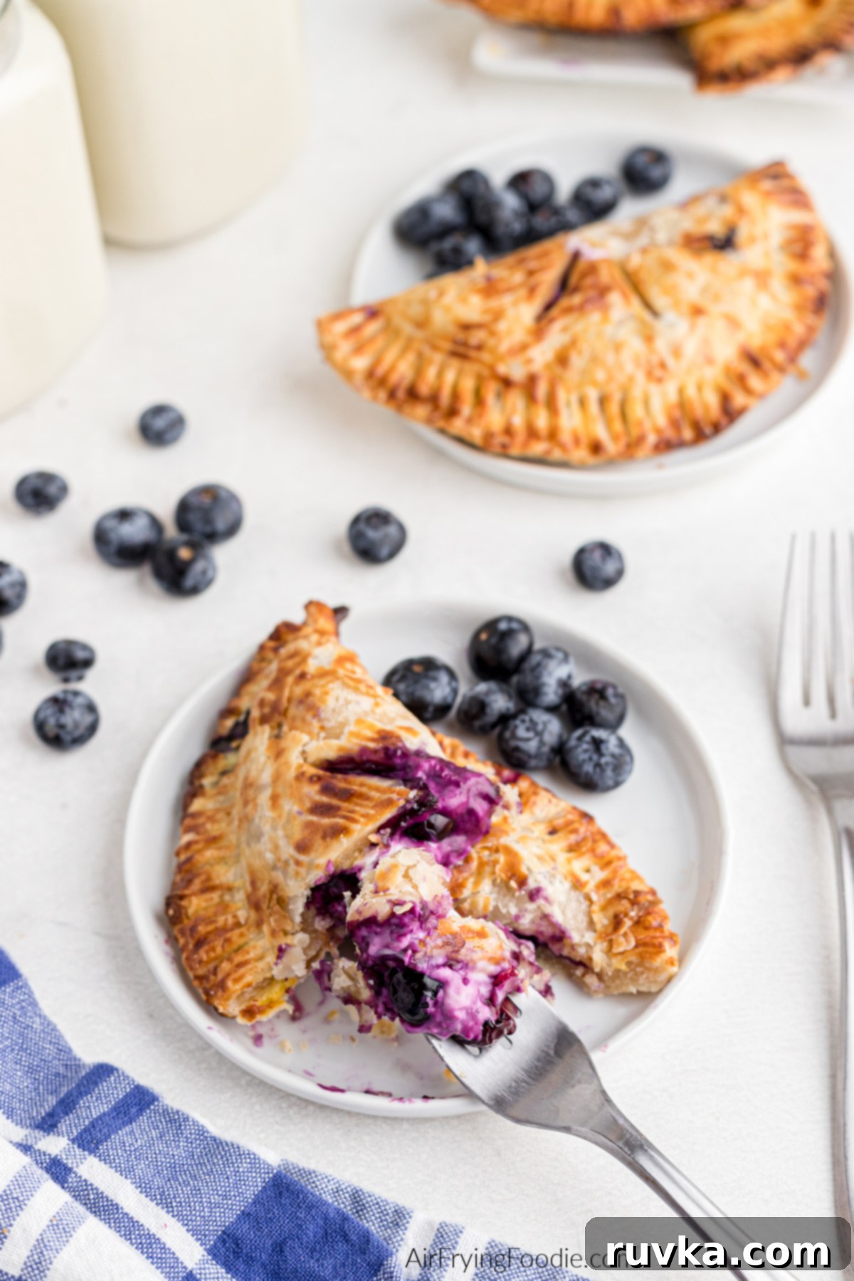 Crispy Air Fried Blueberry Pockets 14 Air fryer blueberry hand pies on plates, one being eaten with a fork