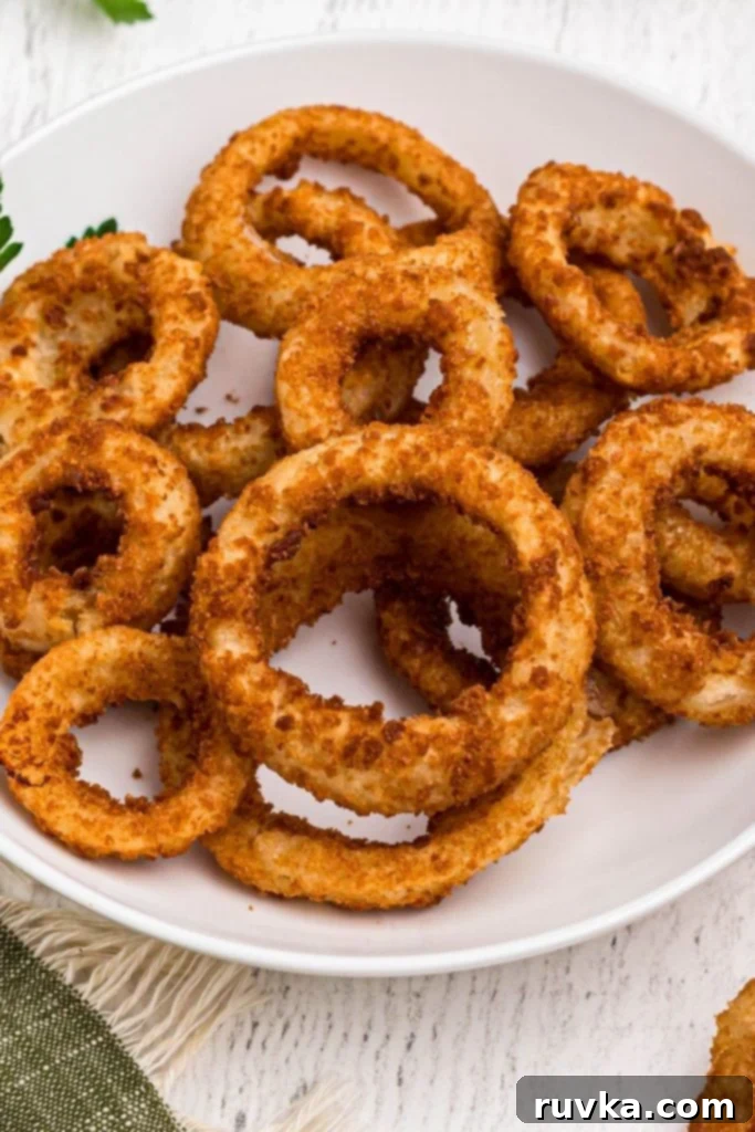 Effortlessly Crispy Air Fryer Onion Rings 2 Golden crispy onion rings stacked on a white plate
