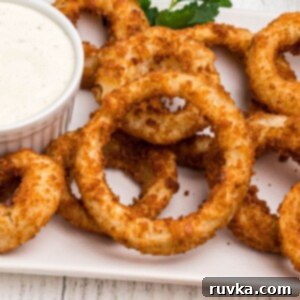 Effortlessly Crispy Air Fryer Onion Rings 7 Golden crispy onion rings on a white plate served with ranch dressing.