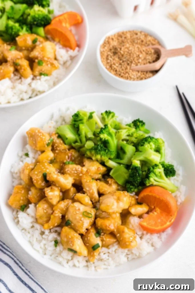 Golden Crispy Air Fryer Orange Chicken 2 Golden orange pieces of chicken covered in orange sauce on a white plate served with rice and broccoli.