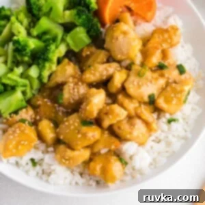 Golden Crispy Air Fryer Orange Chicken 10 Juicy orange chicken served over rice with broccoli on a white plate.