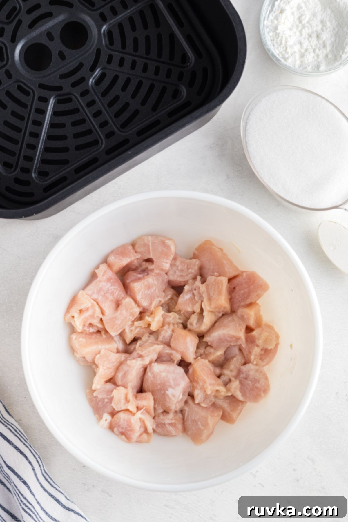 Golden Crispy Air Fryer Orange Chicken 4 Uncooked chicken tossed with cornstarch in a white bowl