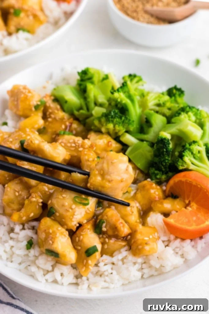 Golden Crispy Air Fryer Orange Chicken 8 Golden orange chicken served over rice and with broccoli on a white plate.