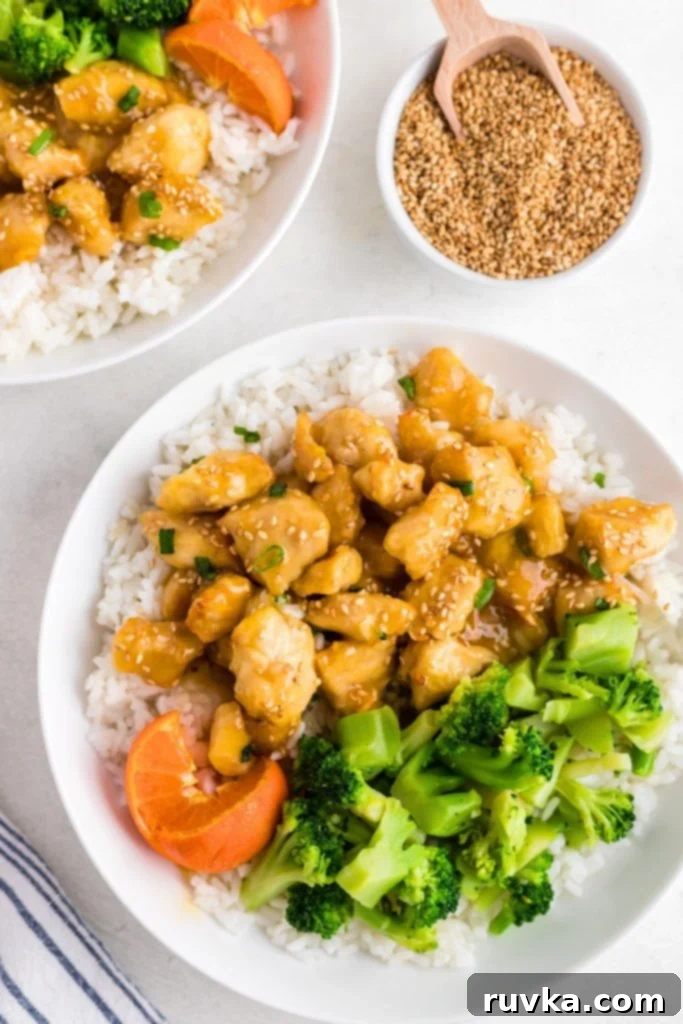 Golden Crispy Air Fryer Orange Chicken 9 Golden orange chicken served on white rice with broccoli and an orange on a white plate.