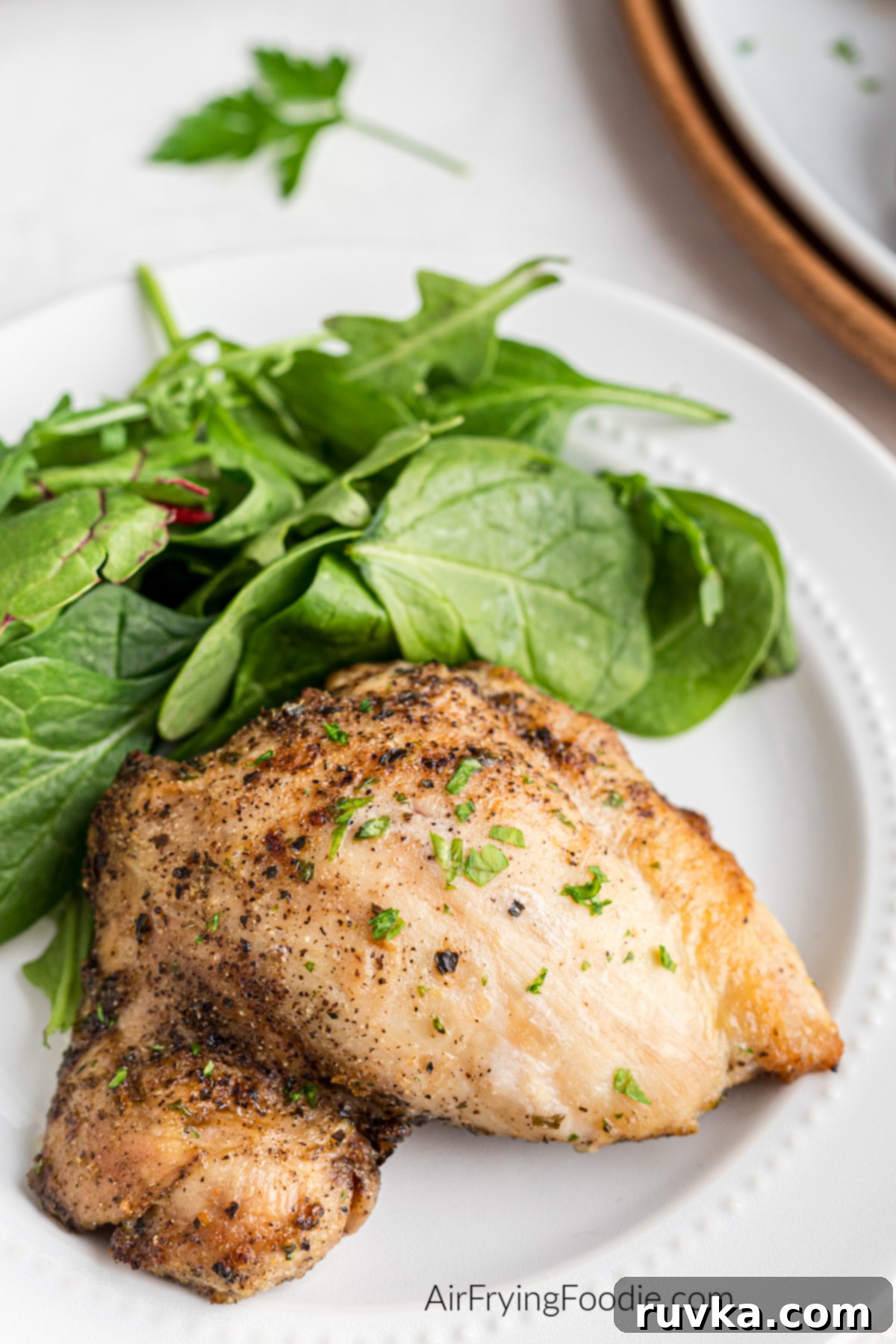 Crispy Air-Fried Chicken Thighs 2 Seasoned boneless chicken thigh made in the air fryer, on a white plate with a side of salad.
