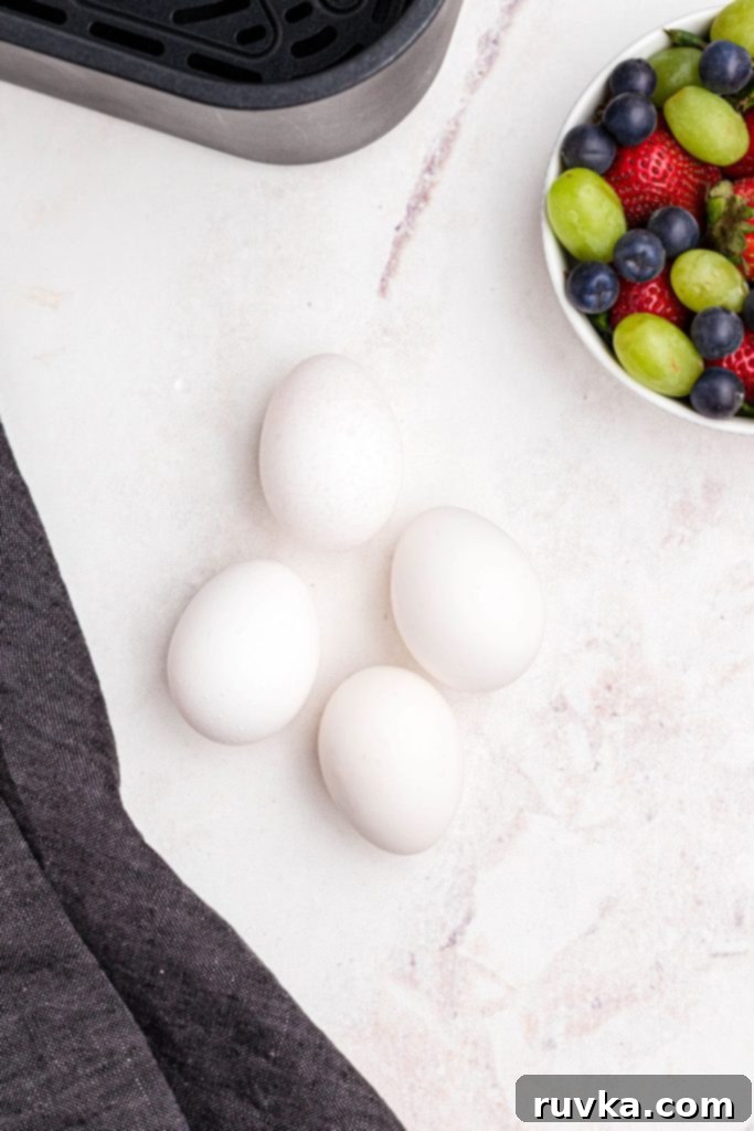 Air Fryer Jammy Eggs 3 Four eggs on a marble table in front of an air fryer basket and a bowl of fruit.