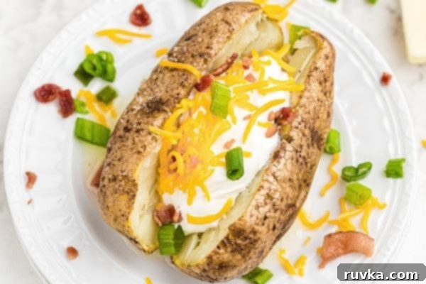 Crispy Air Fryer Loaded Potatoes 2 Baked potato served on a white plate and then topped with sour cream, cheese, crumbled bacon and chopped green onion.