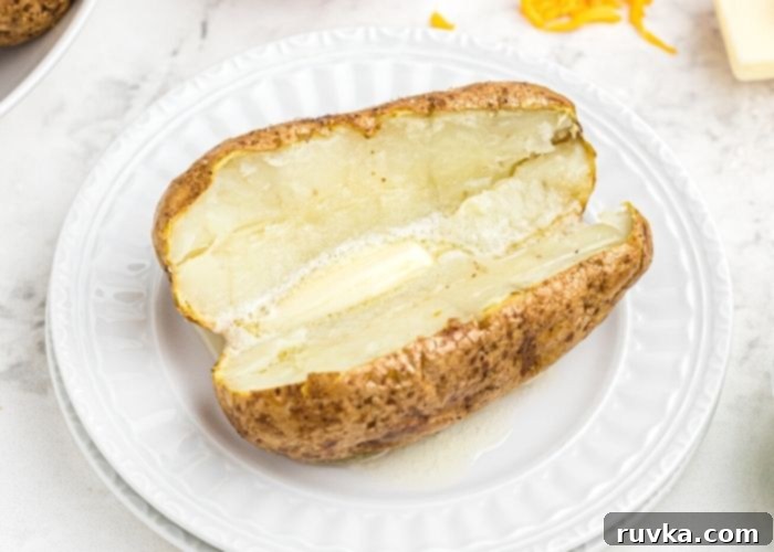 Crispy Air Fryer Loaded Potatoes 3 Baked potato cut open and served with pat of butter on a white plate.