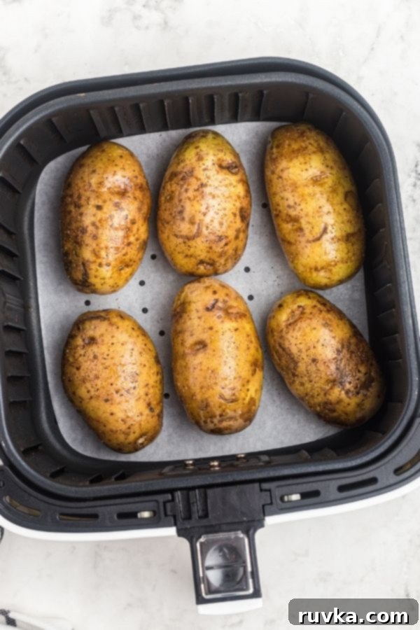 Crispy Air Fryer Loaded Potatoes 4 Potatoes in an air fryer basket on parchment paper before being cooked.