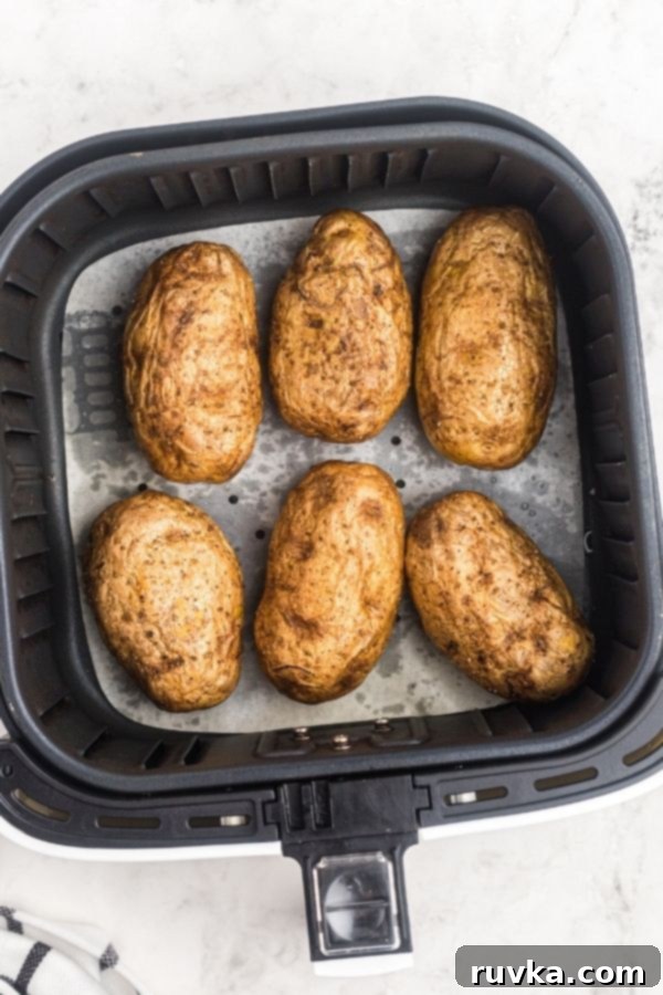 Crispy Air Fryer Loaded Potatoes 5 Cooked potatoes in the air fryer basked on white parchment paper.