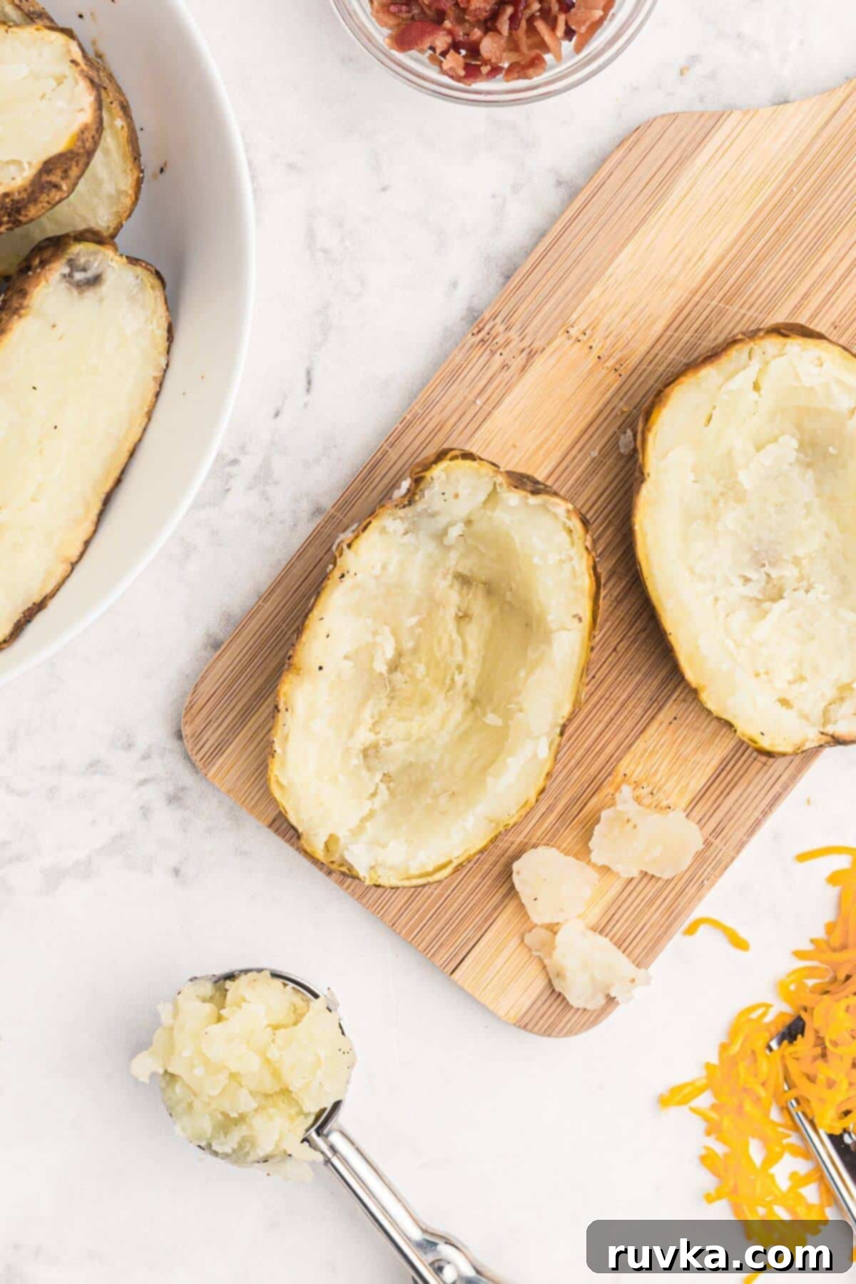 Crispy Air Fryer Potato Skins 3 Baked potatoes sliced in half with centers scooped out on a cutting board.