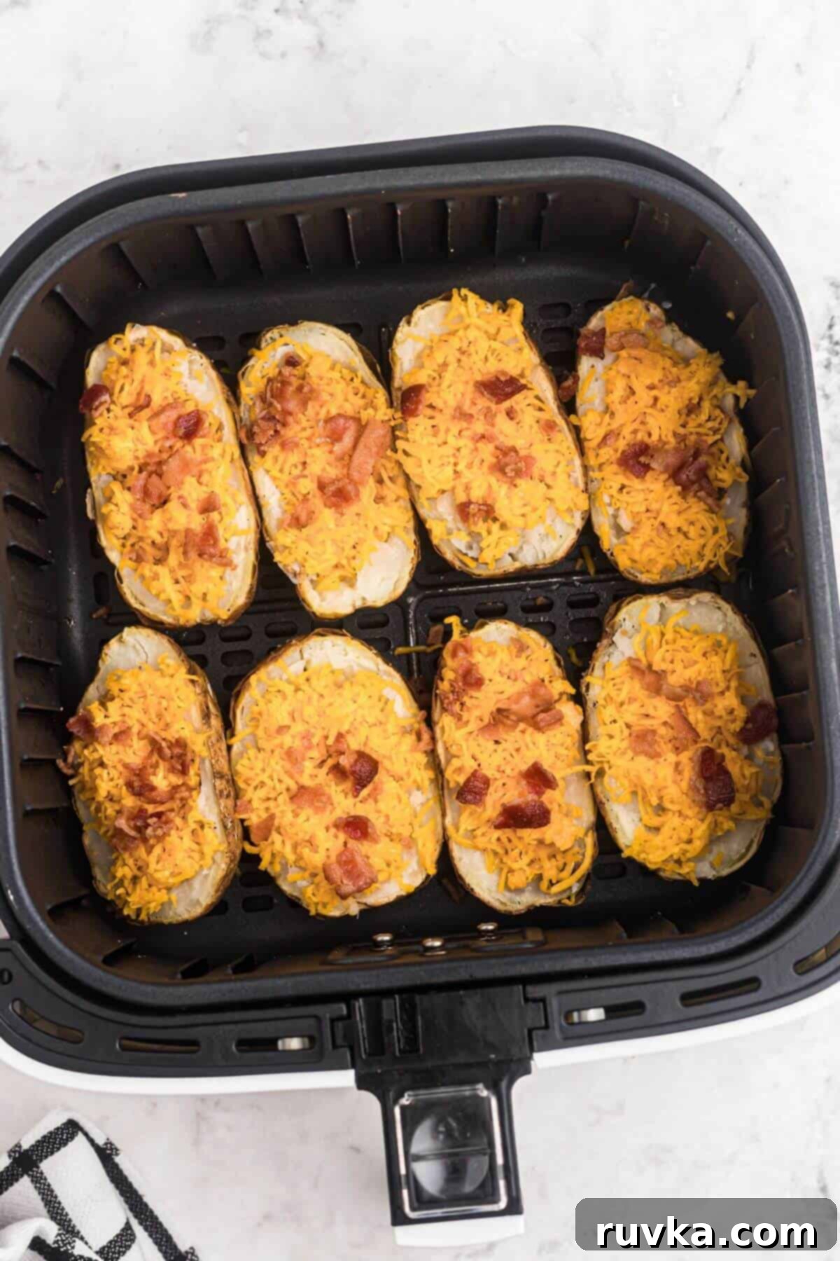Crispy Air Fryer Potato Skins 5 Baked potatoes stuffed with shredded cheese and chopped bacon, placed in the air fryer basket before being cooked.