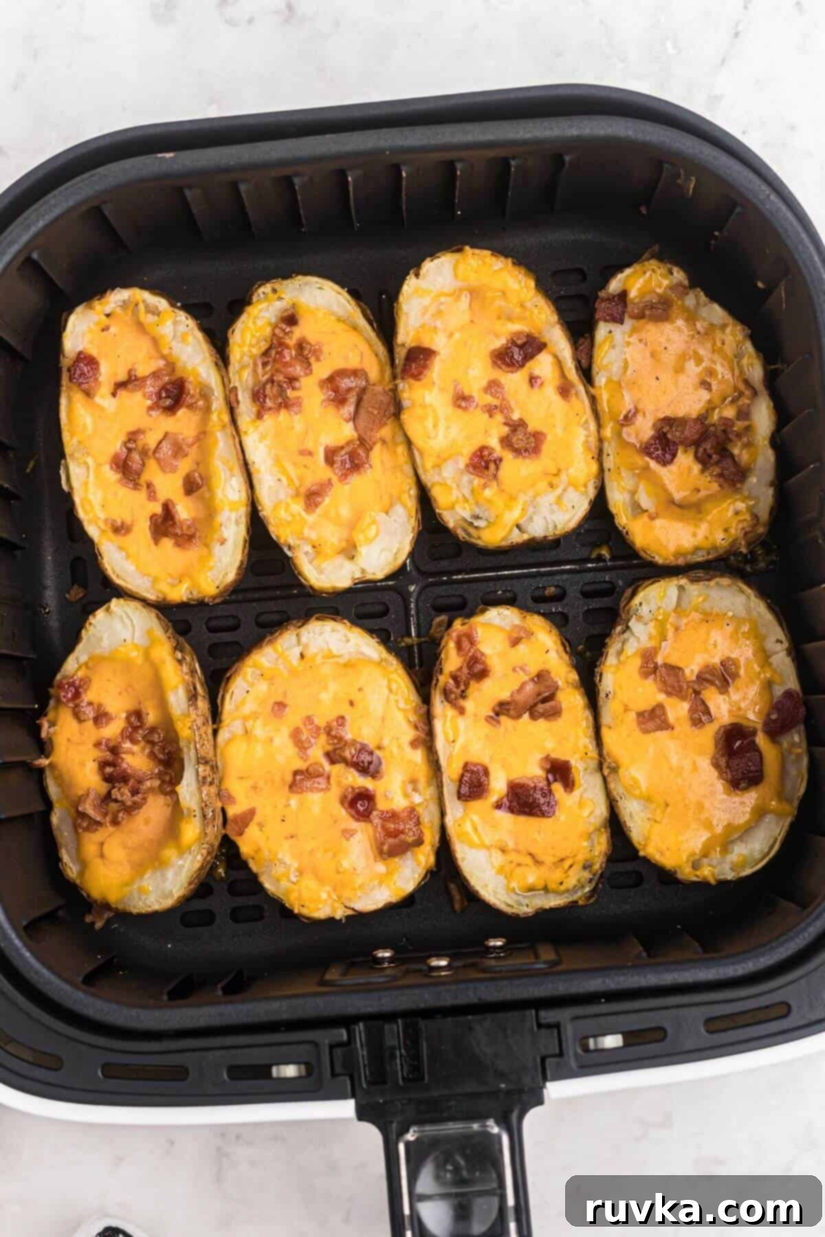 Crispy Air Fryer Potato Skins 6 Baked potatoes stuffed with shredded melted cheese and chopped bacon, placed in the air fryer basket after being cooked.