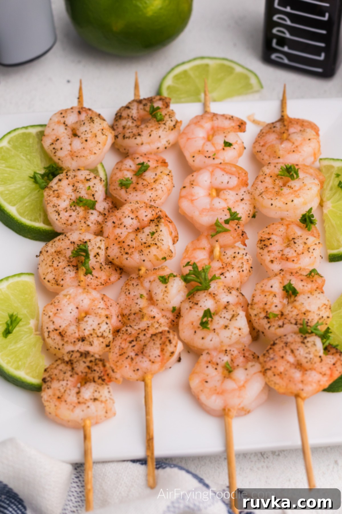 Easy Air Fryer Shrimp Skewers 6 Air fried shrimp skewers on a white plate with sliced of lime.
